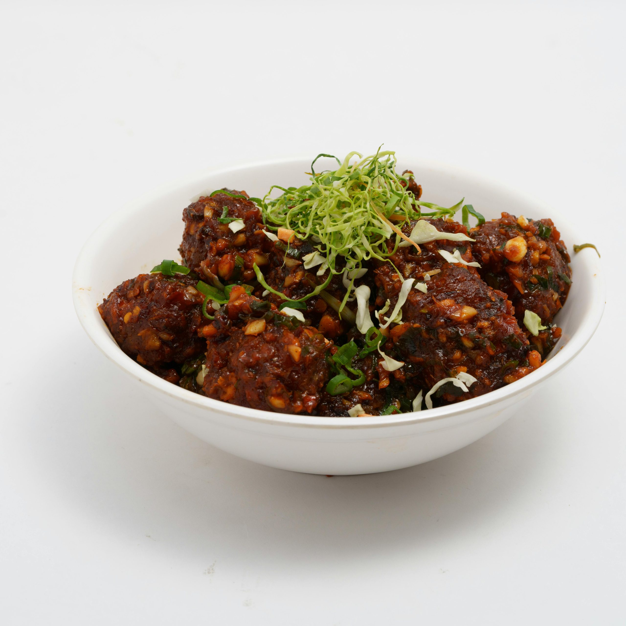 Savor the flavors of spicy Manchurian balls garnished with fresh greens in a white bowl.